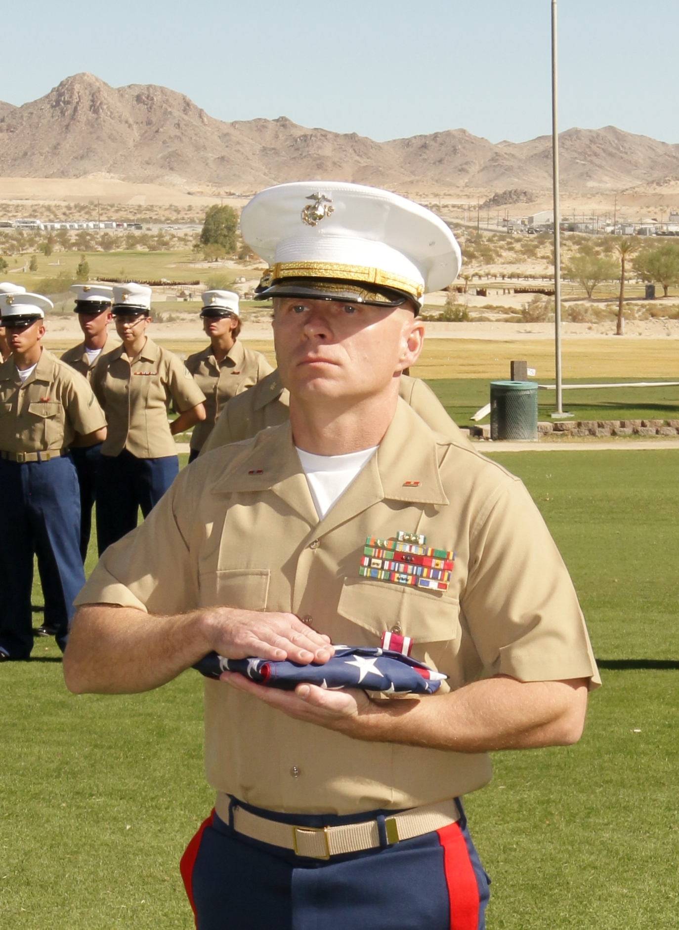 Jon stands in uniform with folded American flag. 