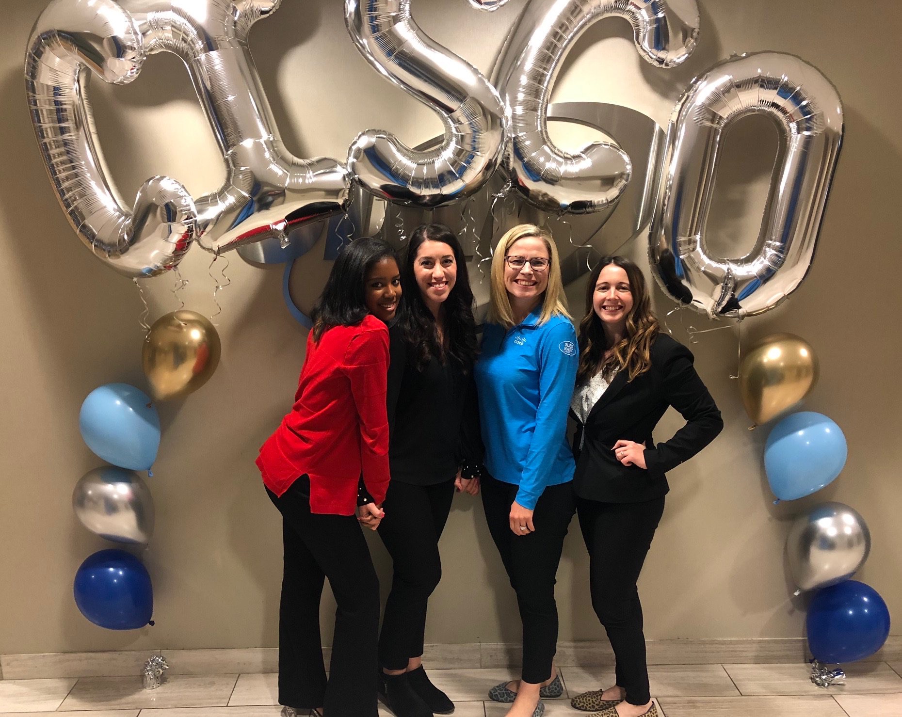 Bree stands with three peers under large silver balloons spelling out CISCO.