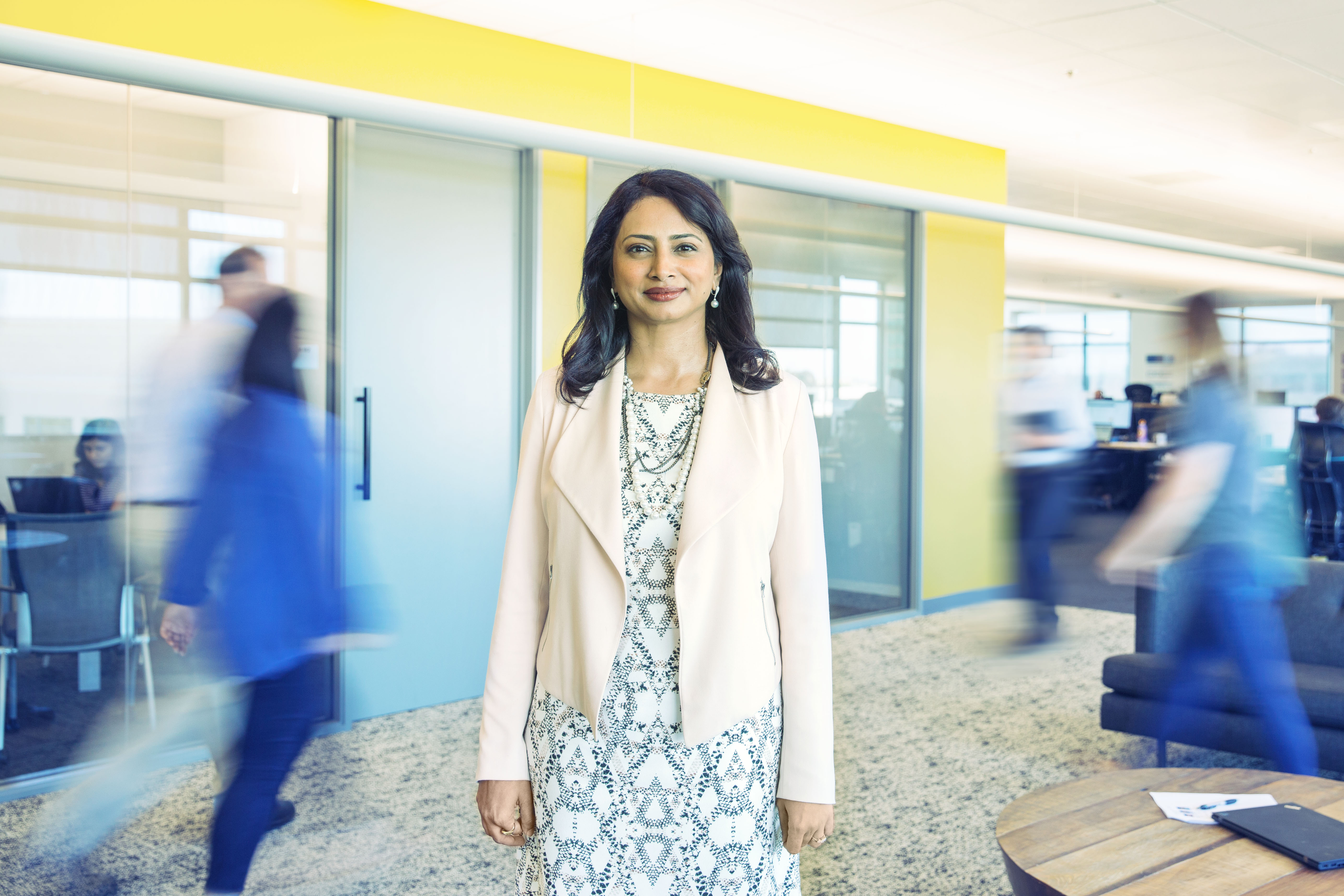 Varsha stands in a Cisco office as people around her are blurred in motion.