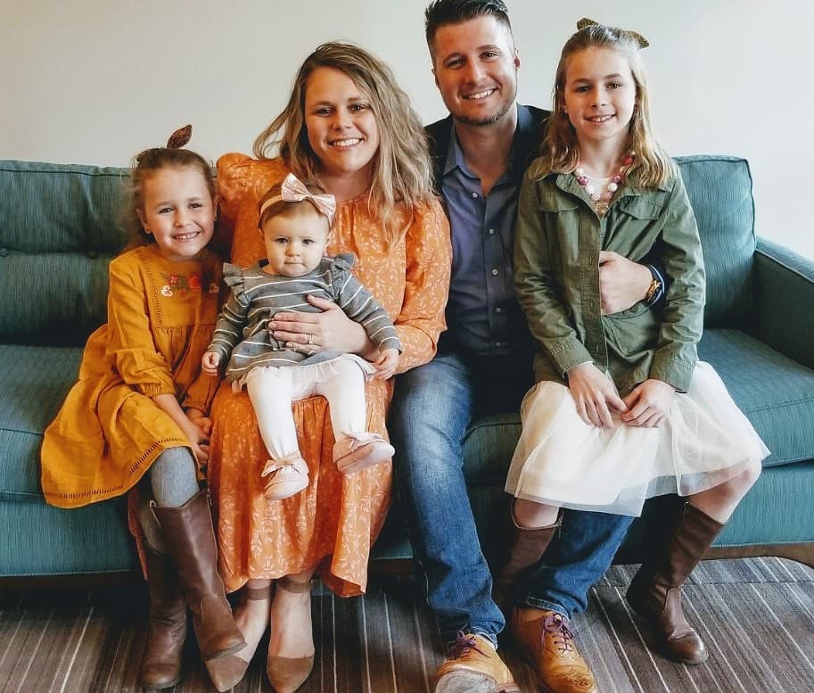 David, his wife, and their 3 daughters smile for the camera on a couch.