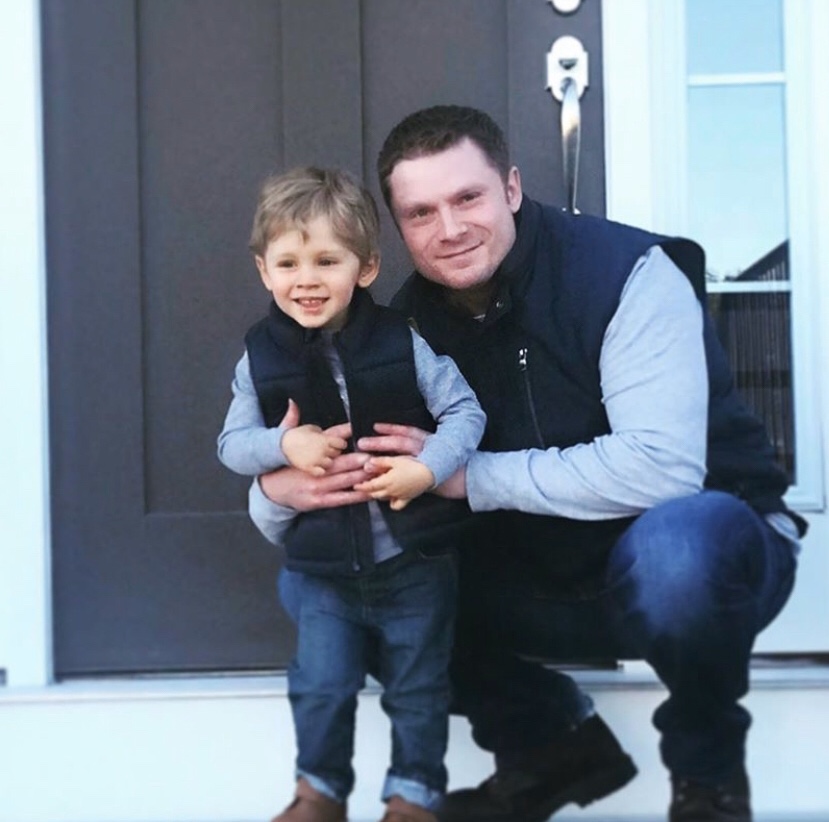 Sara's husband and son wear matching jeans, grey tshirt, and navy vests for a picture.