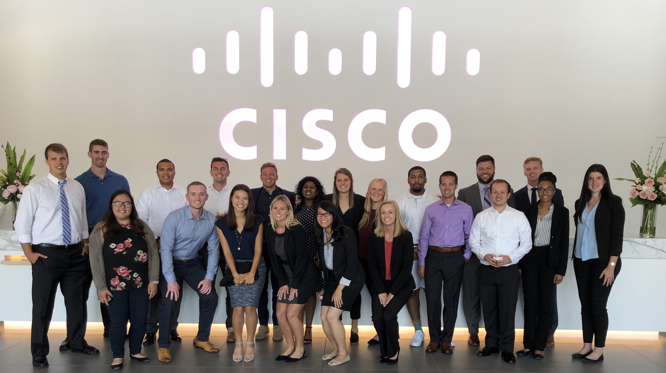 Julain and his teammates stand in a lobby under a giant lit Cisco logo on their first day of onboarding.
