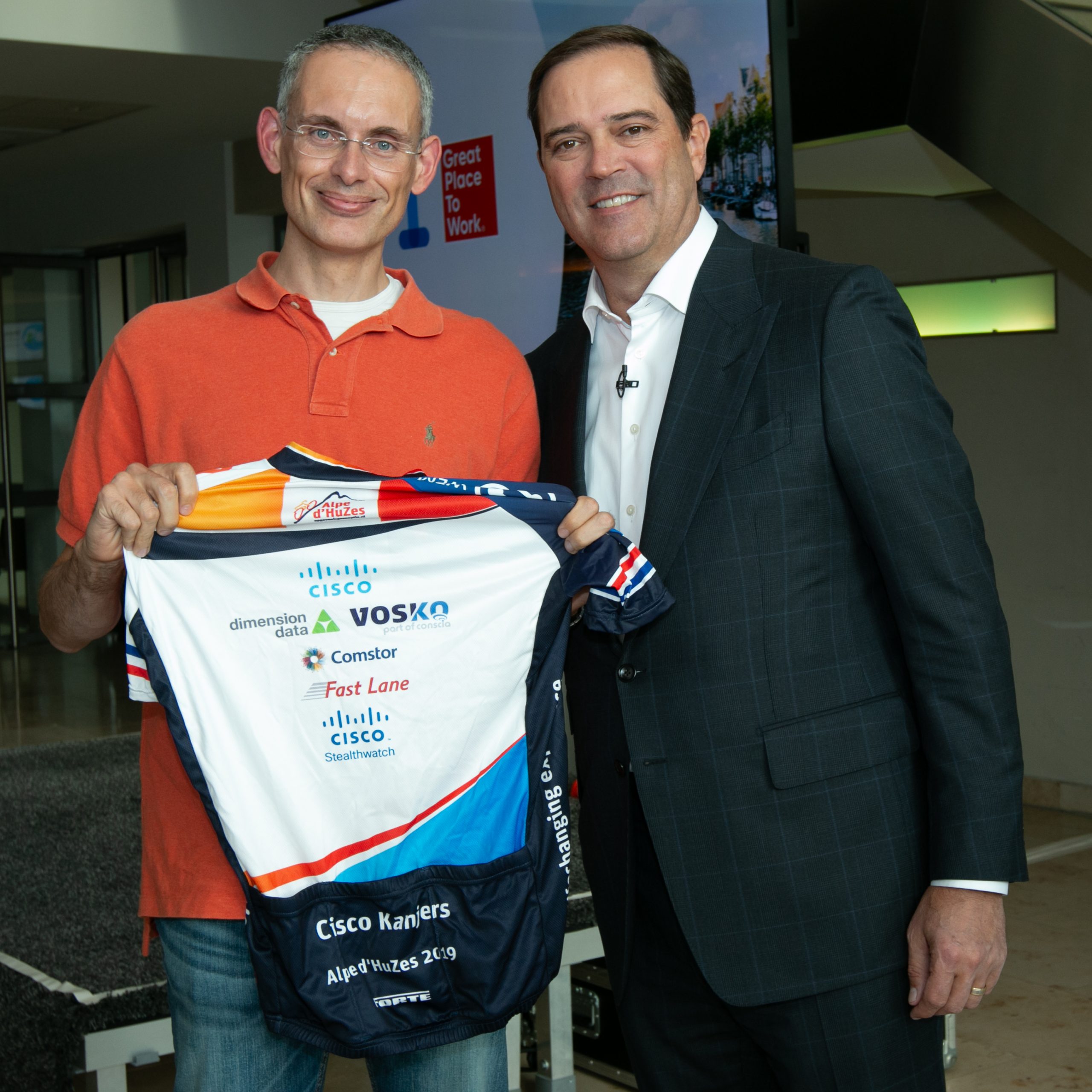 Mark holds his biking shirt smiling next to Cisco CEO Chuck Robbins.