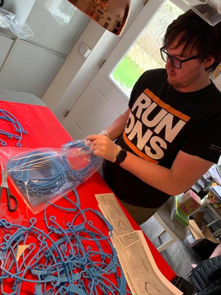 Ollie sets up the work station at home, packing away blue visor fastenors into plastic bags.