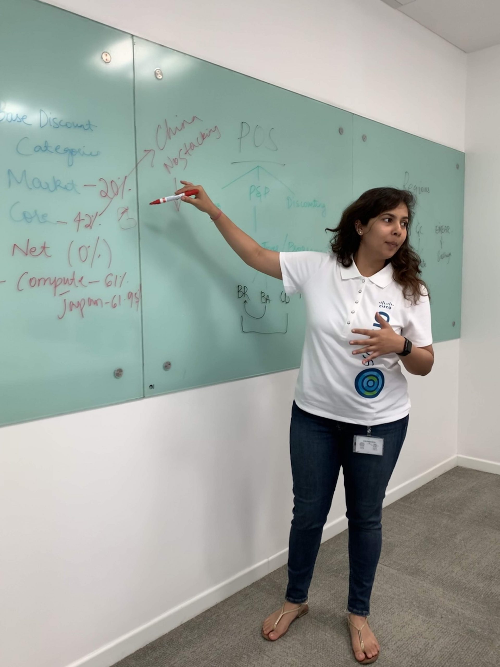 Nikita wears a white Cisco polo and is standing writing on a white board while instructing people watching.