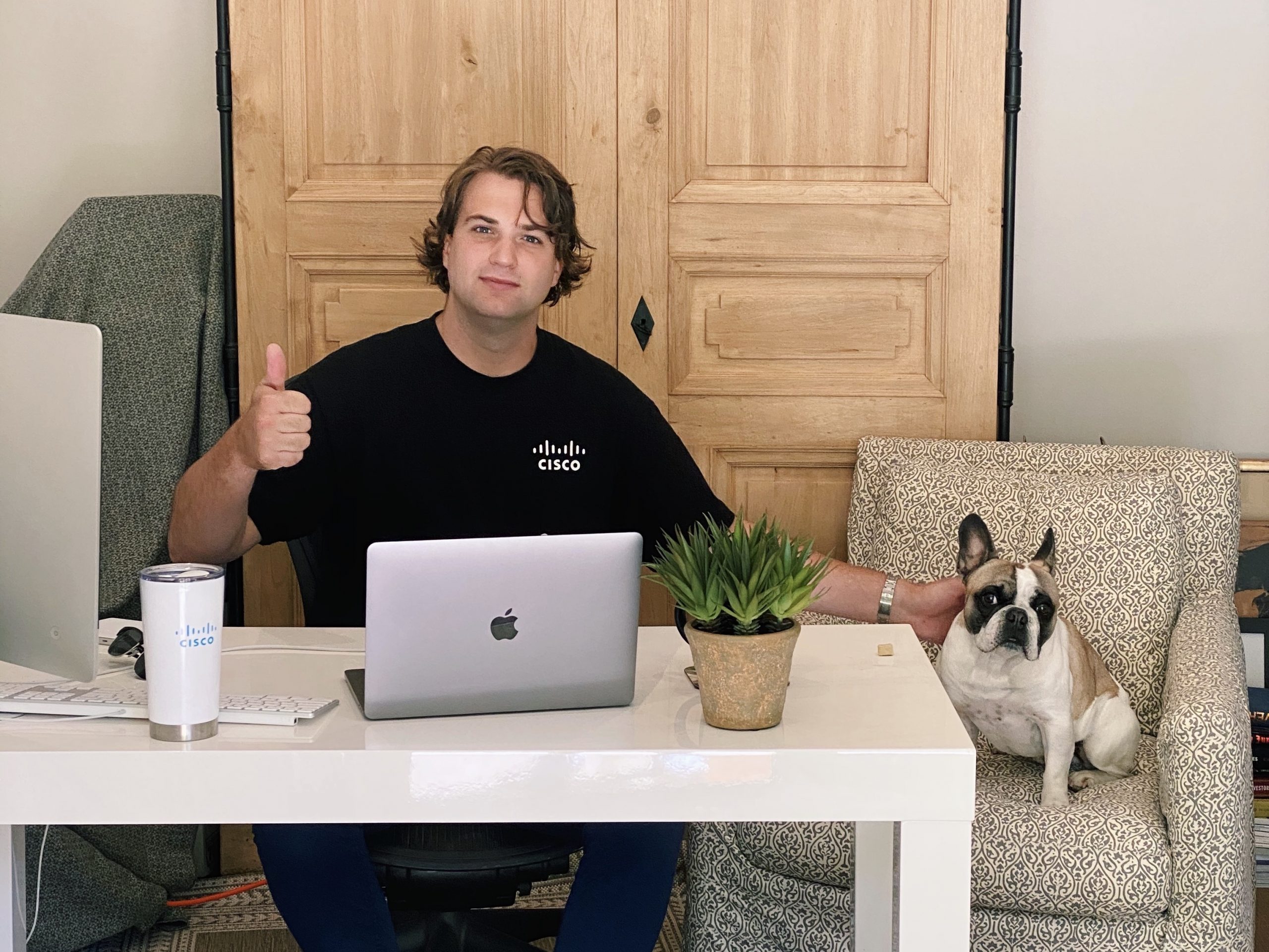 Matthew and his French Bulldog, Winston, sitting at his desk at home with his laptop open and signing a thumbs up.