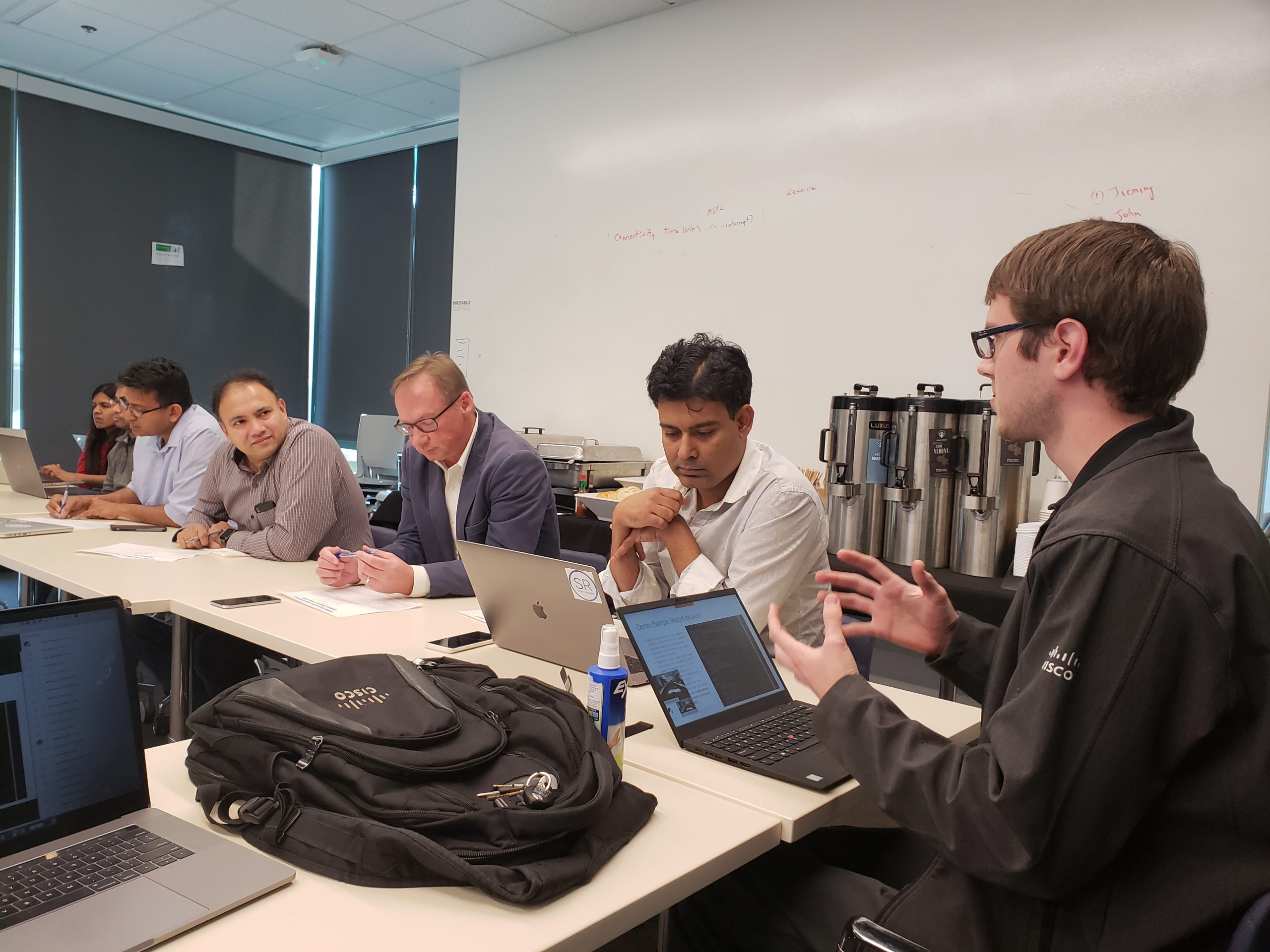 6 people sit in a conference room during a tech talk.