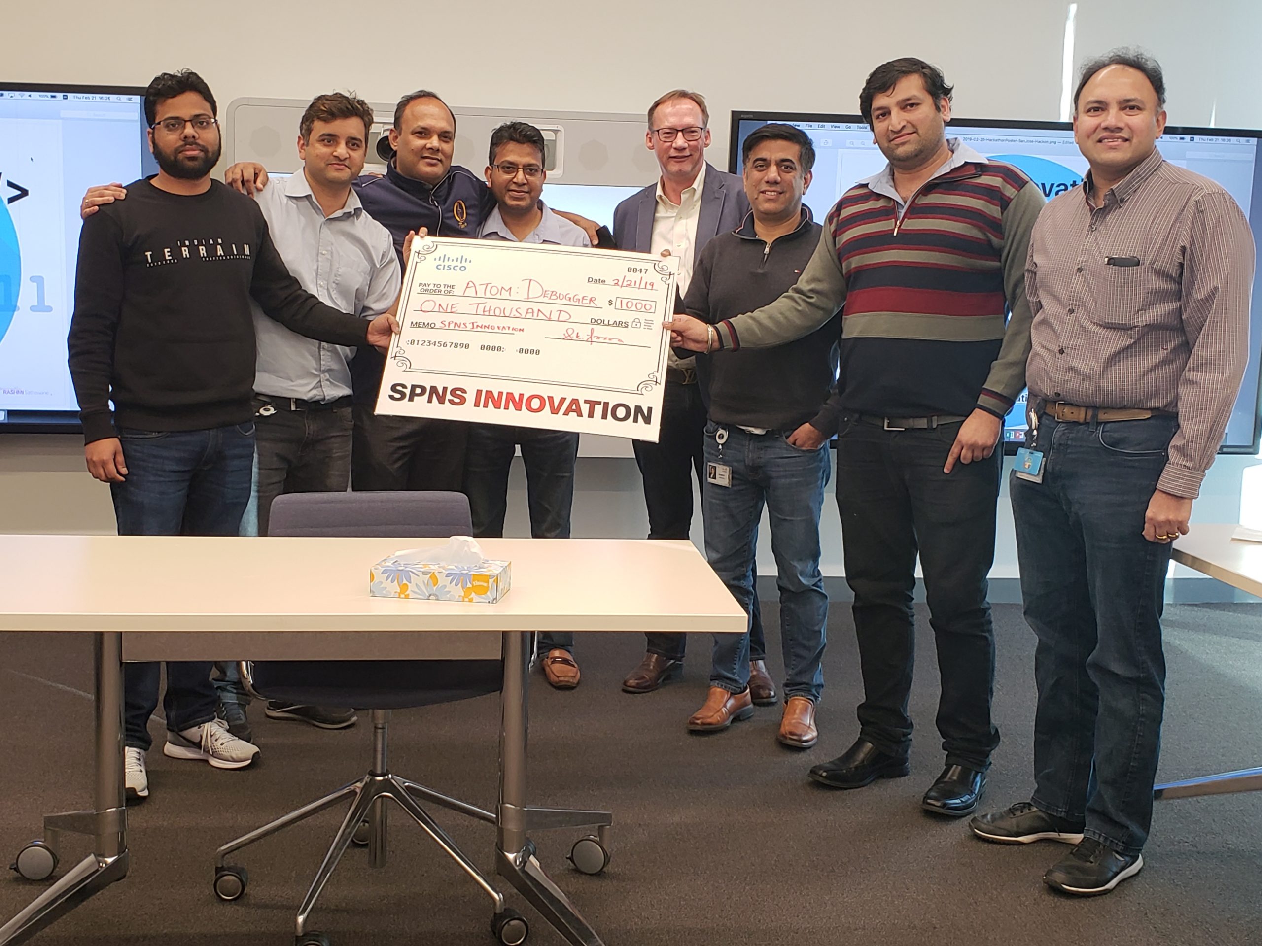 A group of Rashmi's friends and colleagues holding a large check with the words SPNS INNOVATION across the bottom.
