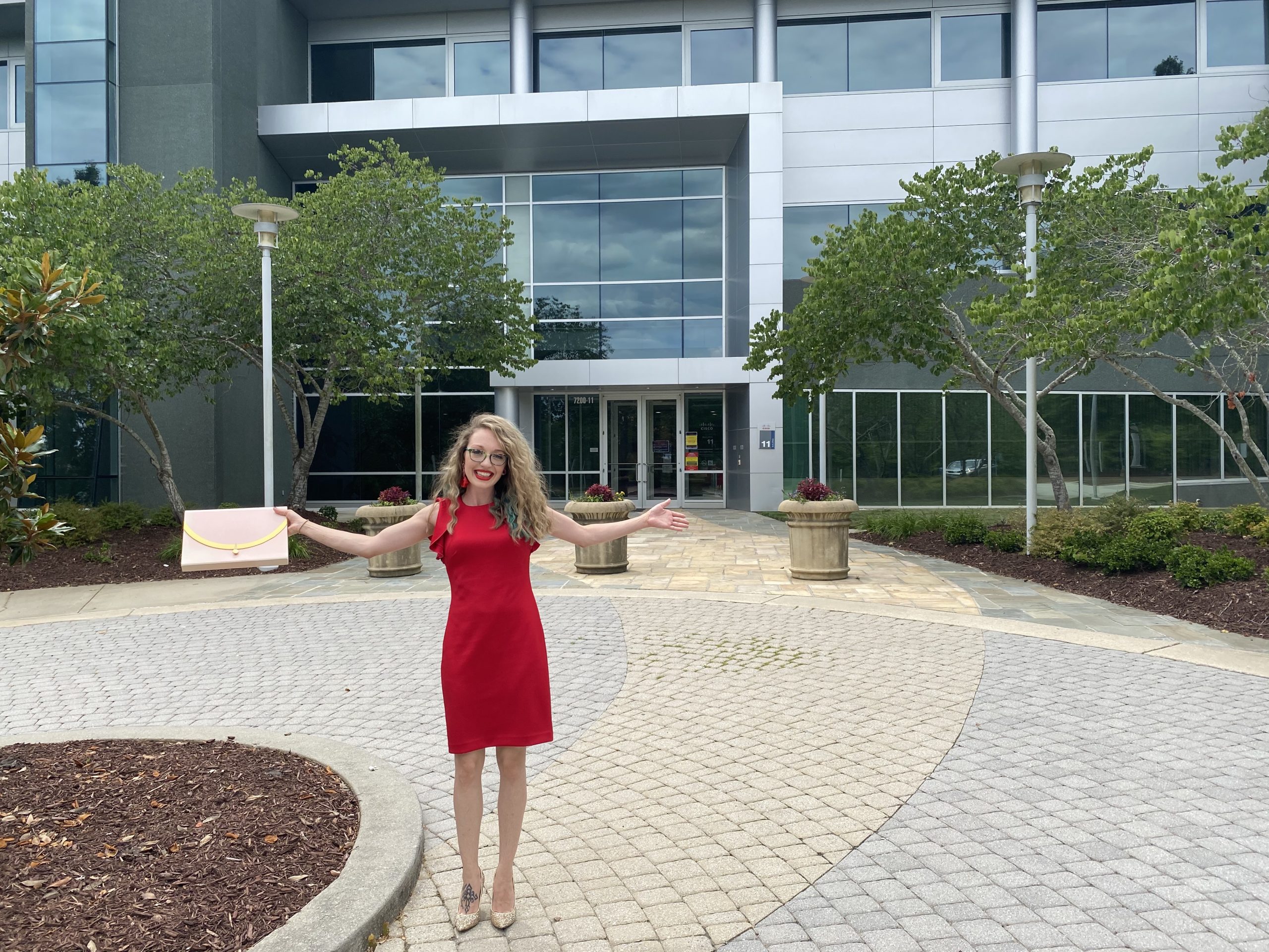 Miranda holds out her arms and shares a big smile in front of a Cisco building in RTP.