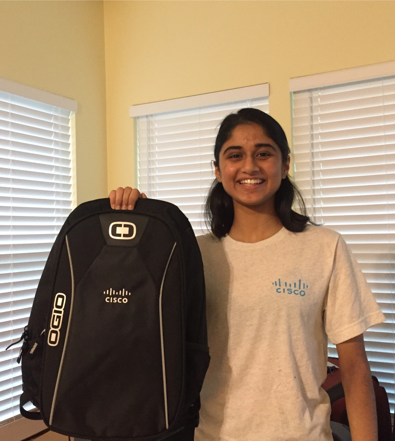 Jessica holds up her new Cisco branded backpack while wearing a Cisco t-shirt at home.