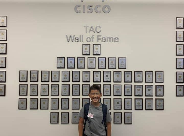 Nic's oldest son smiles in front of the Cisco TAC Wall of Fame