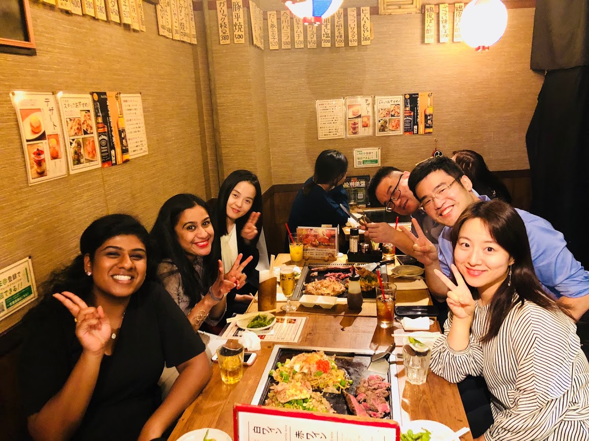 Prabha and her team hold up peace signs with their hands at her birthday team dinner.