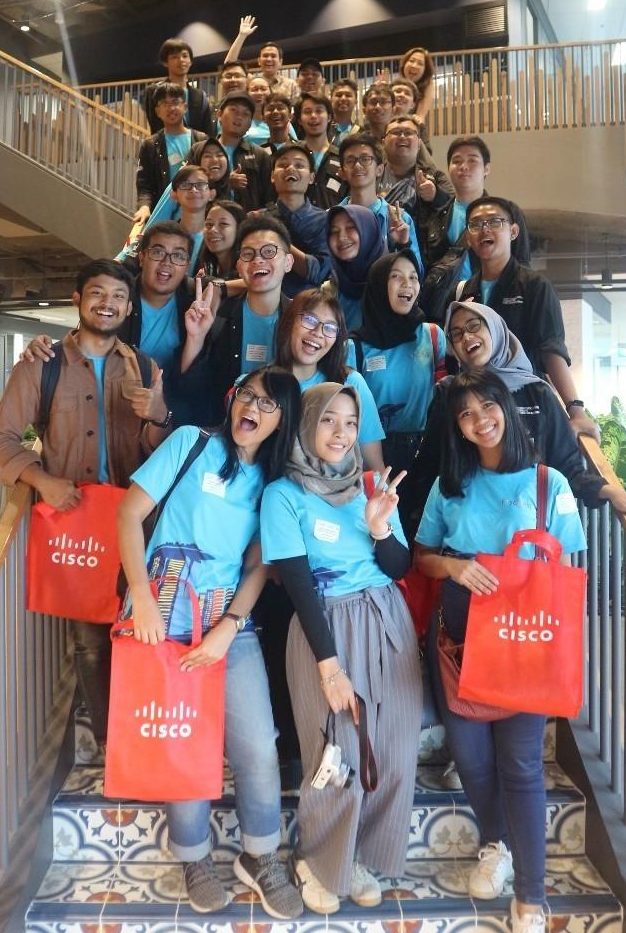 Students from the University in Indonesia smile on a staircase holding Cisco bags.