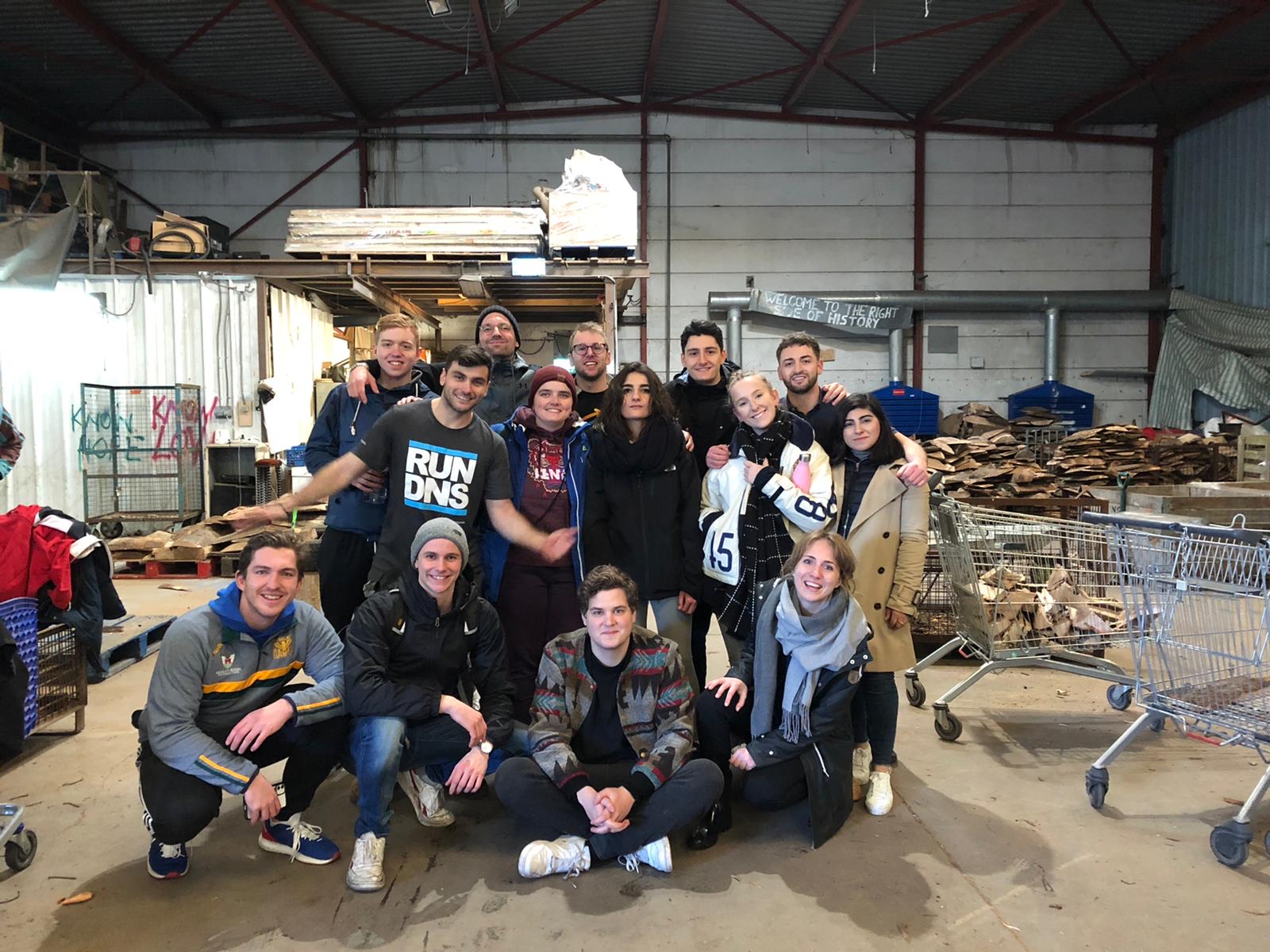 The group of graduate volunteers standing and sitting together in one of The Jungle warehouses.