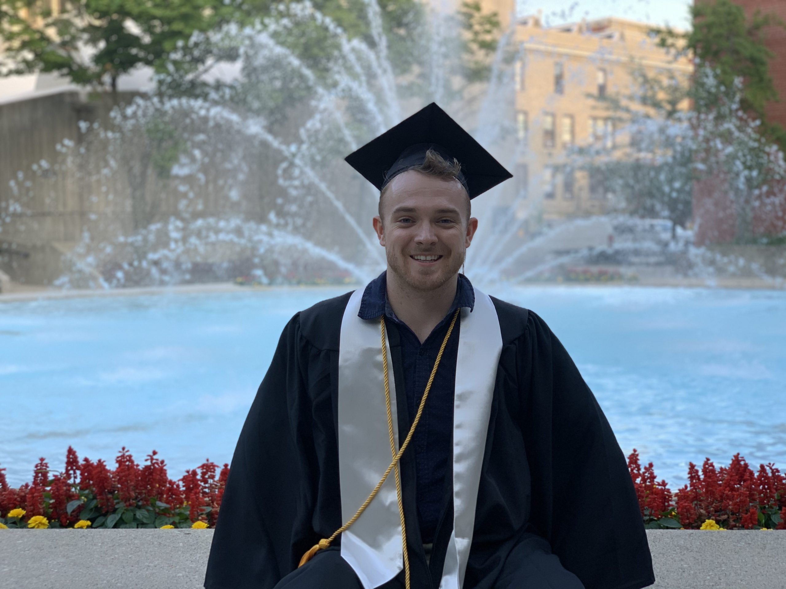 Nathan in cap and gown sitting in front of fountain. 