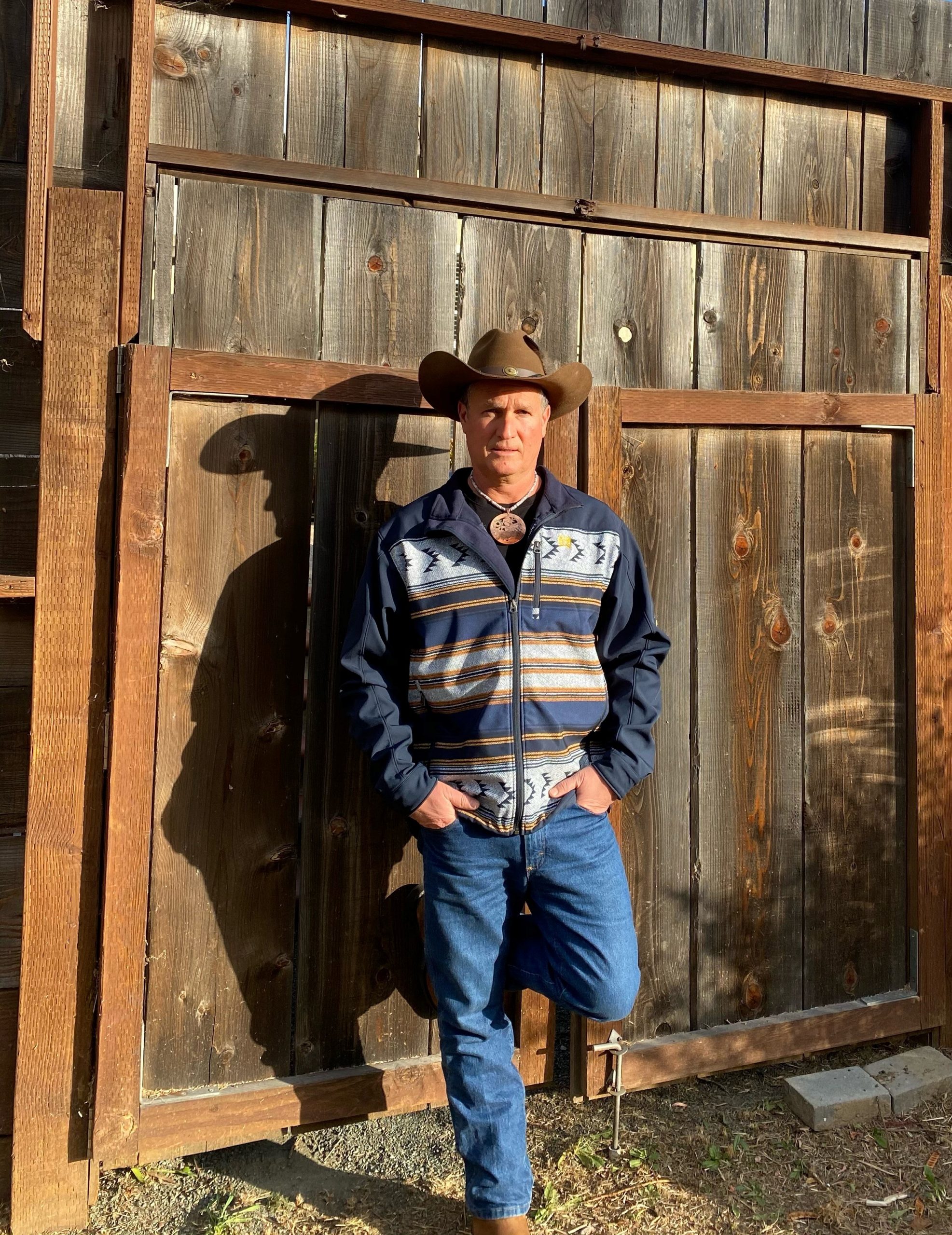 Ken Twist wears a hat and stand against a wooden board background.