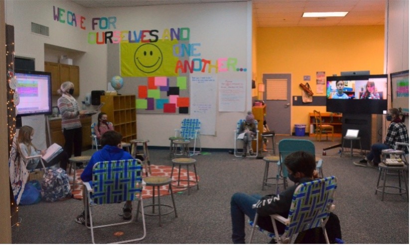 hybrid classroom with students sitting in fold out chairs and teacher instructing using Webex