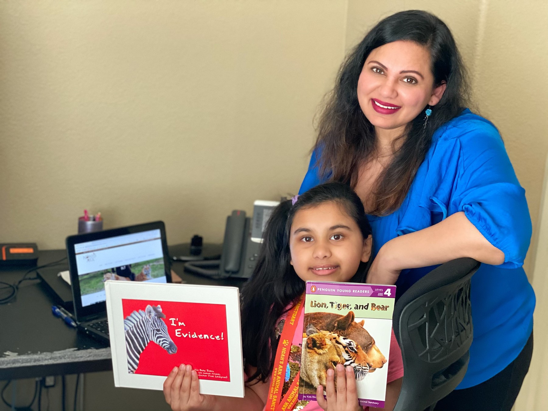 Karishma stadning behind her daughter, while she holds up books that she's read