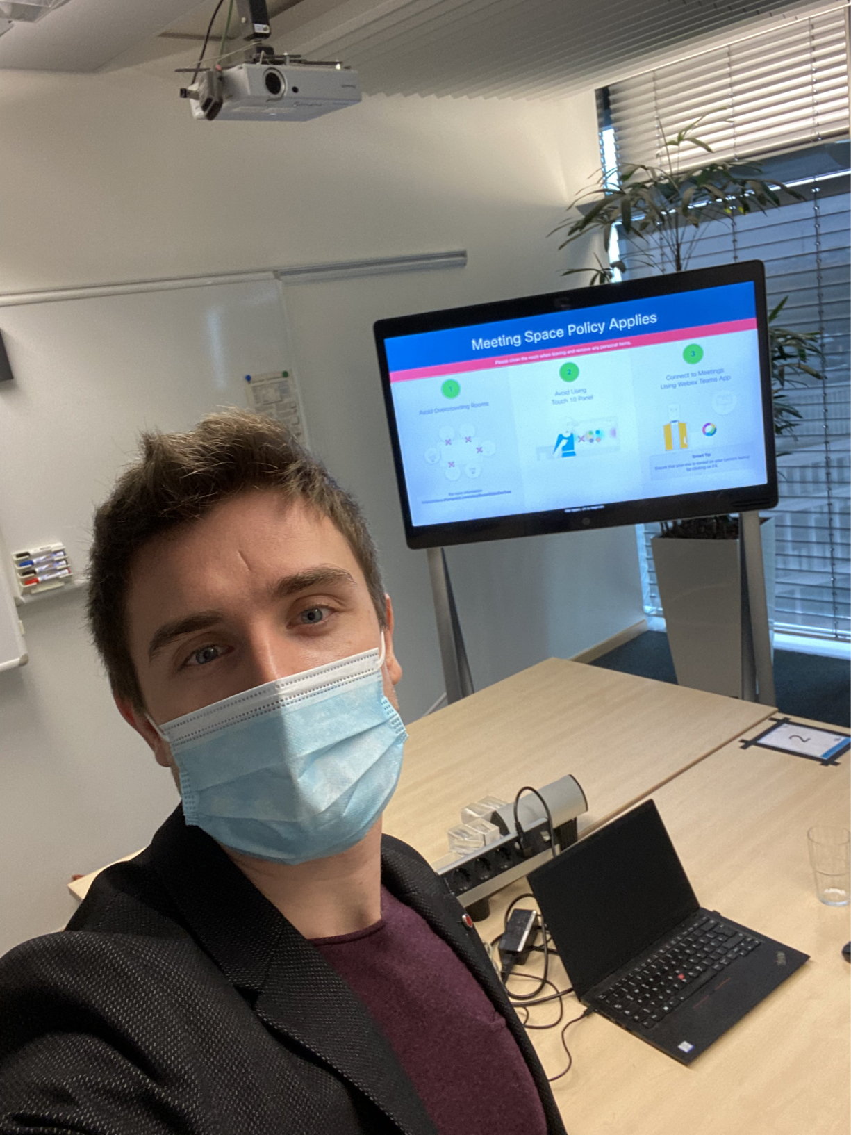 Marwin taking a selfie in a conference room, with a mask on.
