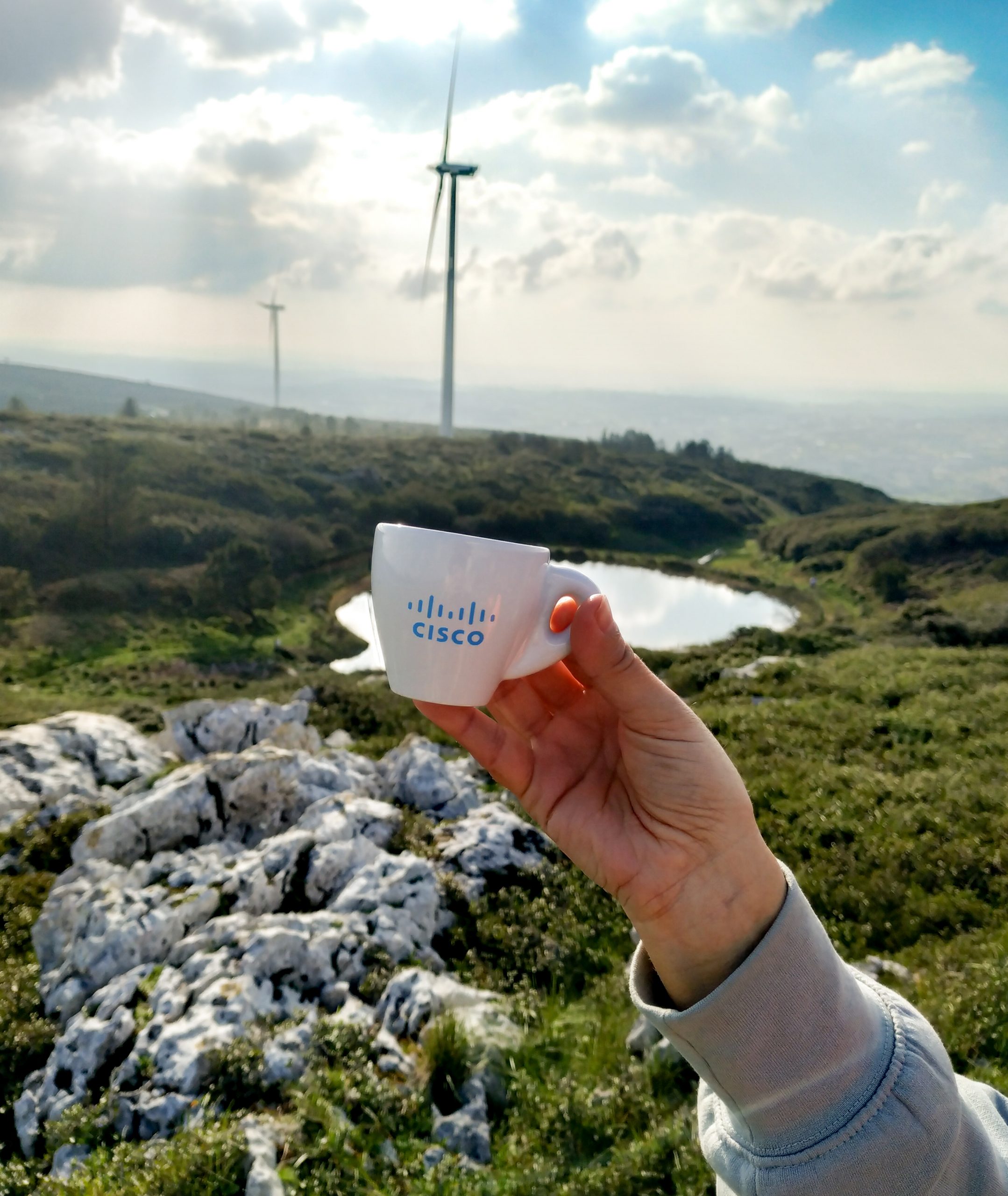 Holding up espresso cup overlooking grassy hills and rocks.