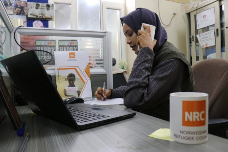 A woman using a cell phone while sitting in front of a laptop