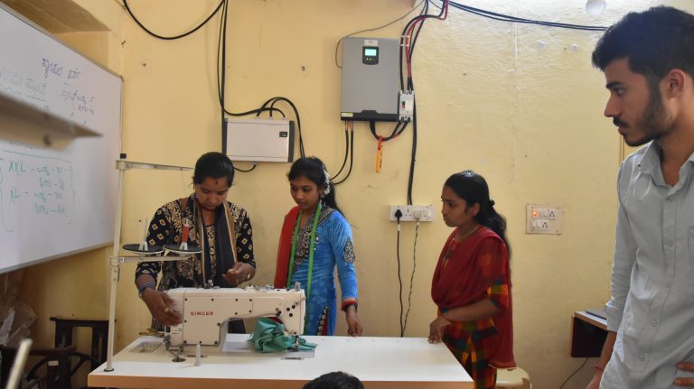 Three women standing in front of a sewing machine with a man standing off to the side
