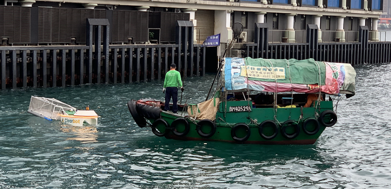 A robot picking up trash in the ocean next to a boat