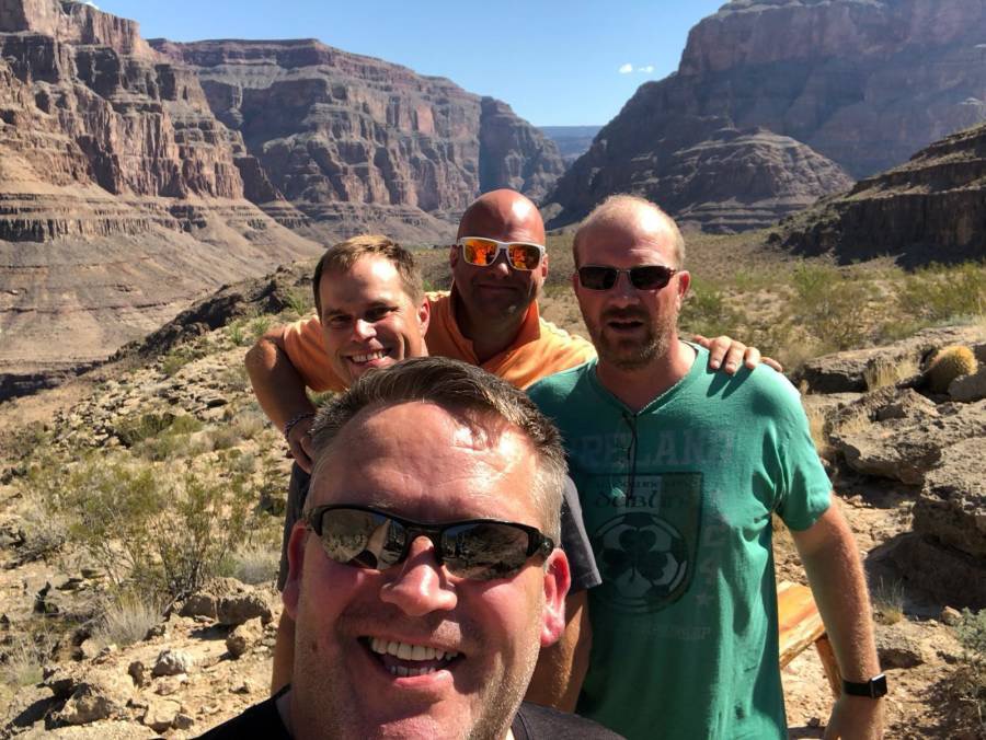 Selfie of four men stand smiling with a mountain range behind them.