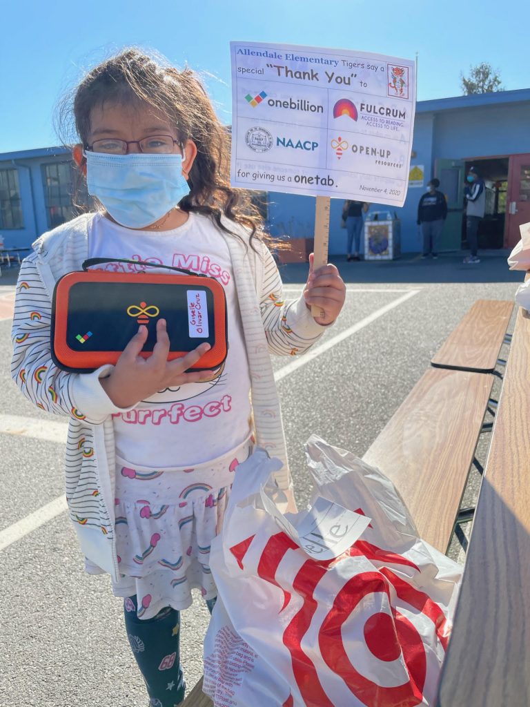 A little girl wearing a mask and holding up a sign