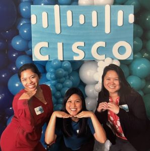 three women pose in front of balloons and Cisco logo