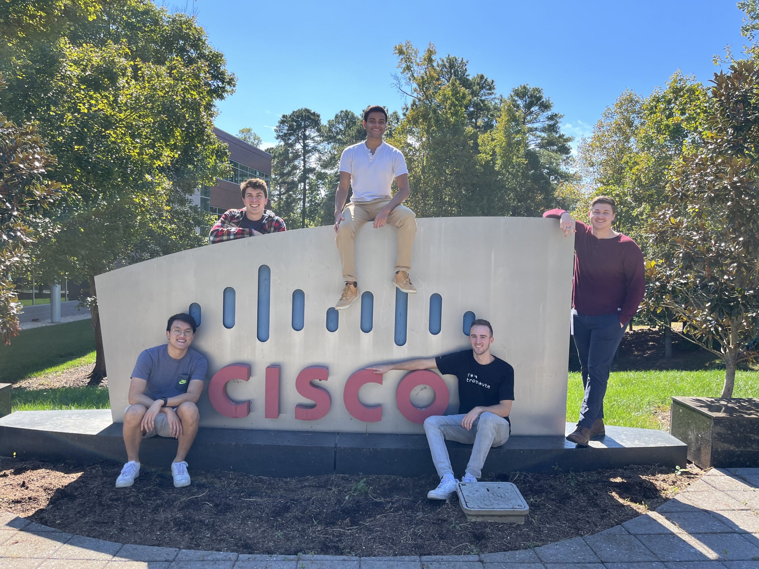 5 people sit around the Cisco logo outside.