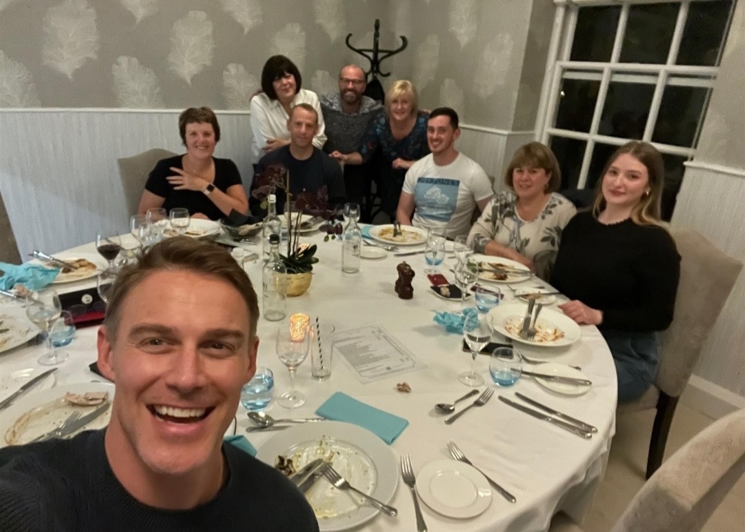 Jessie Pavelka selfie and team behind him at dinner table.