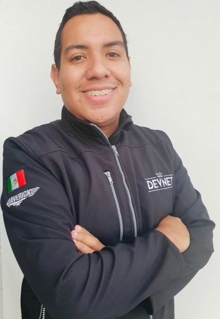 Emmanuel with smiling at camera with arms crossed wearing DevNet jacket.