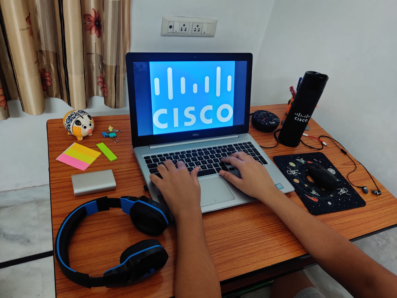 Desk with headphones, sticky notes, mouse and mousepad, and laptop in the center with man's hands typing.