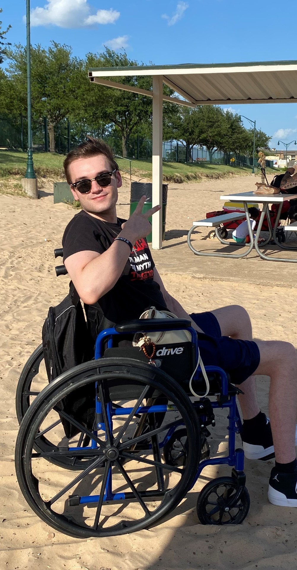 Man in wheelchair wearing sunglasses, holding hand up in peace sign.