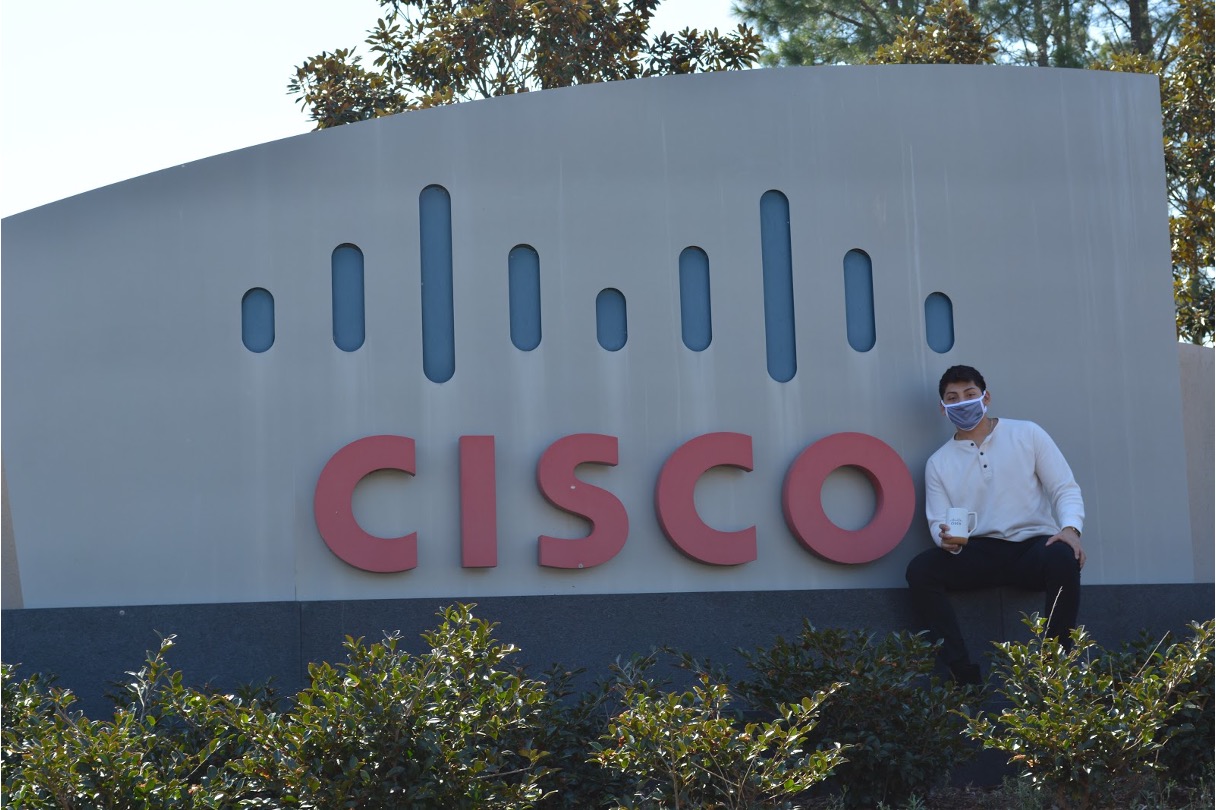 Cristopher sitting in front of a Cisco sign.