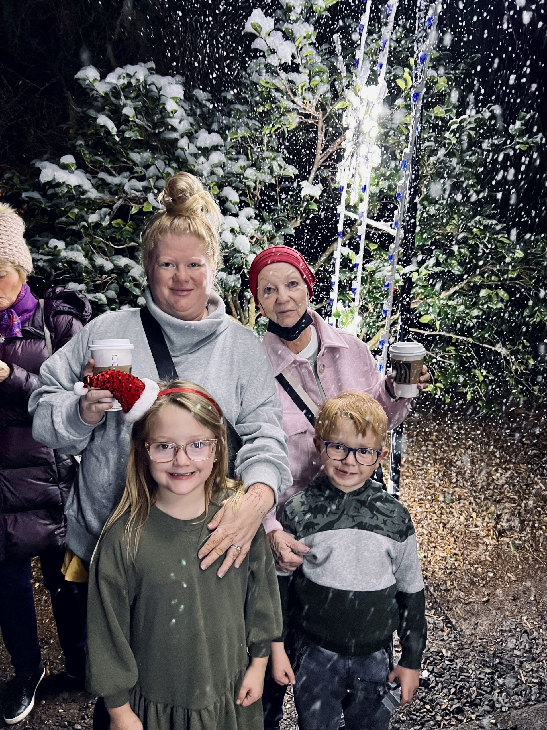 Mike Rausch's wife, mother-in-law, and two children stand together. They are wearing winter clothing and there is snow falling around them. 