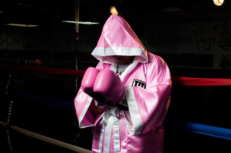 Chechey W. in a boxing ring wearing a pink robe and boxing gloves.