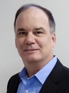 A man wearing a blue collared shirt and black jacket.Ned Bagno is on the GEMS team and manages the EnergyOps program