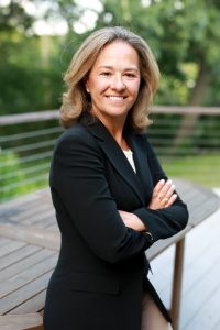 A woman wearing a black suit, sitting outside.