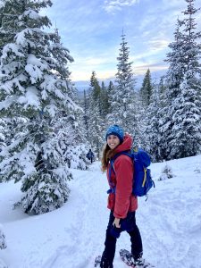 A woman in a red jacket, snowshoeing through a forest in winter