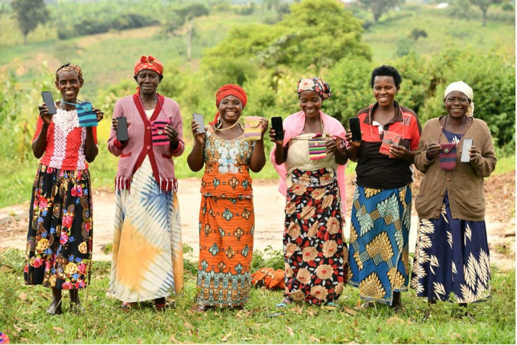 Women from the Rwamwanja Refugee Settlement in Uganda standing side by side in colorful clothing, holding up their phones
