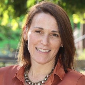 A woman in an outdoor setting, smiling at the camera.