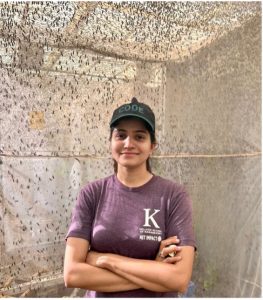 A young women, smiling with her arms crossed, wearing a t shirt and baseball cap