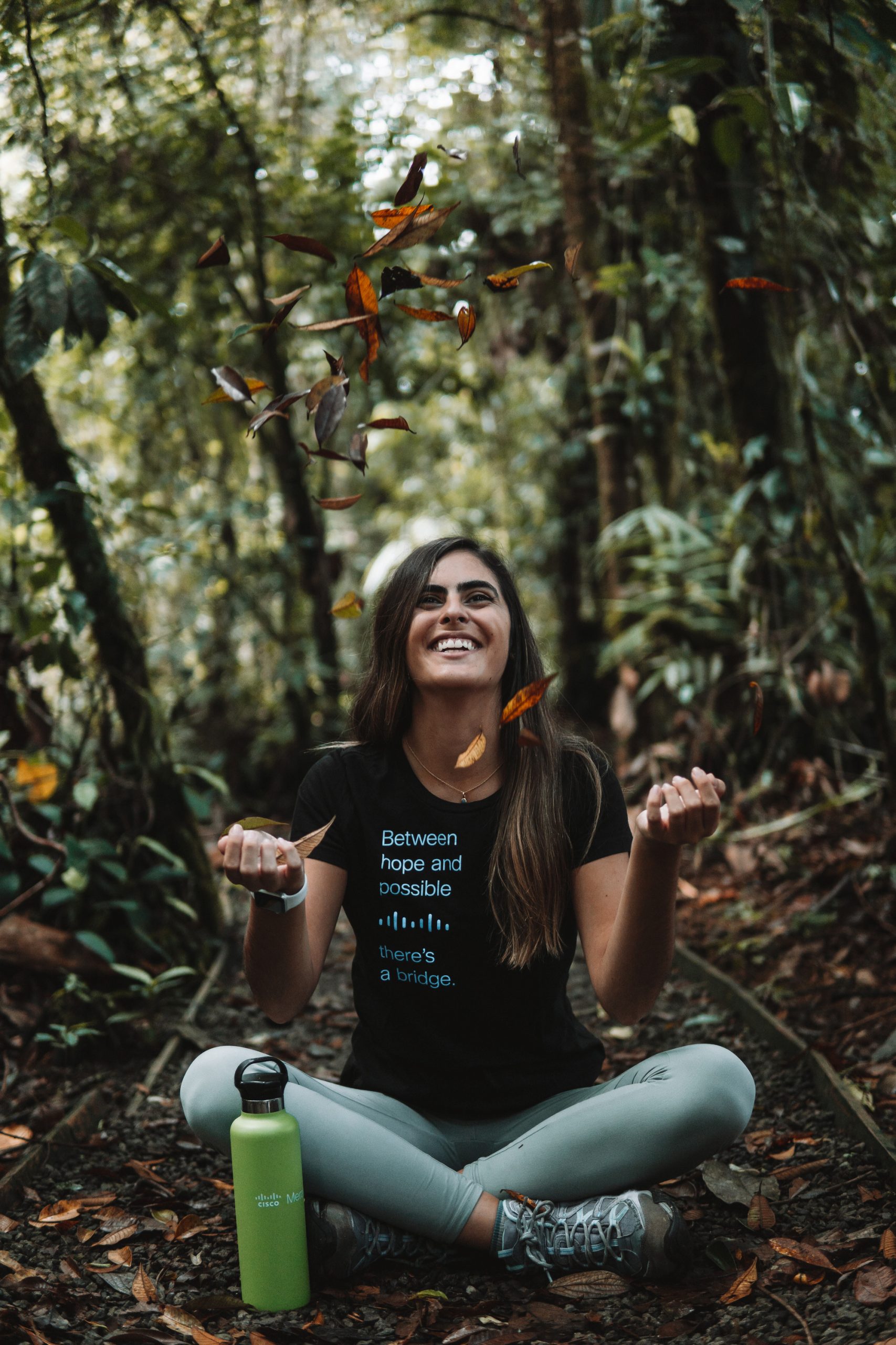 Lucero F. sits in nature wearing a Cisco shirt and throws leaves in the air.