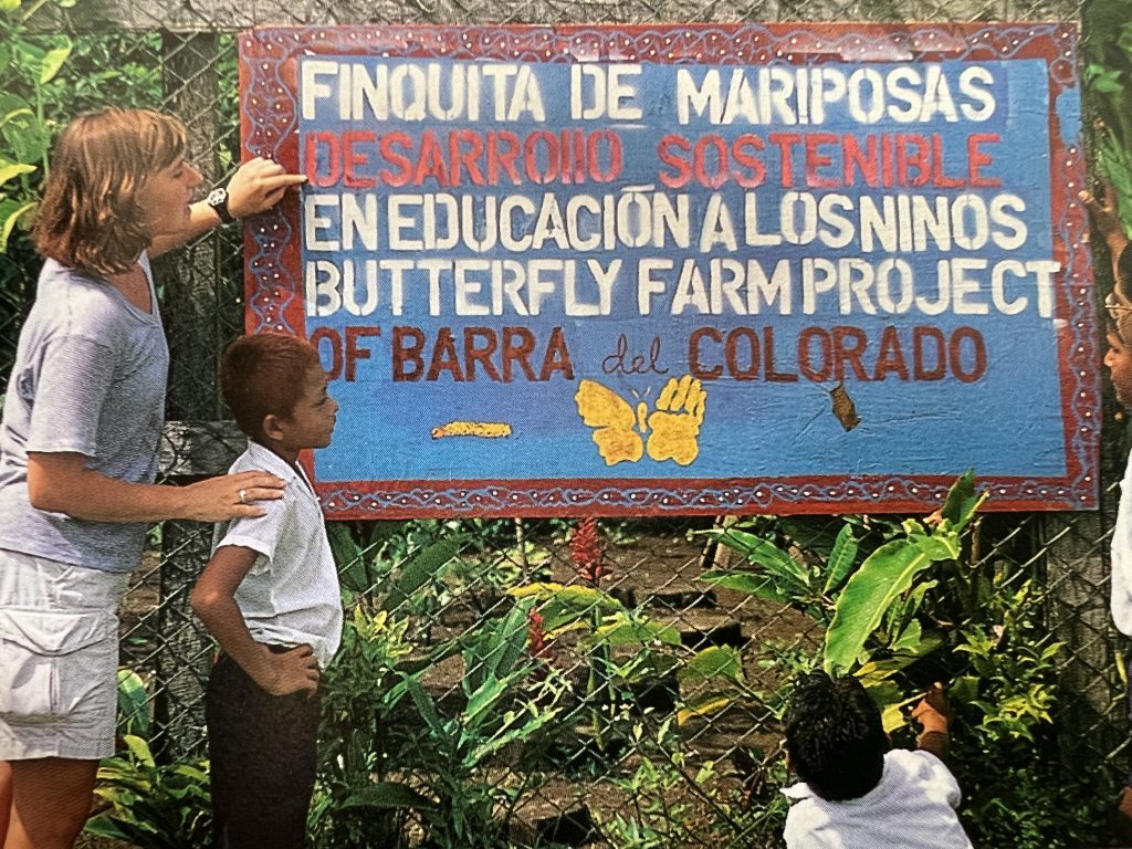 A woman posing with 2 children near a sign with Spanish words on it.