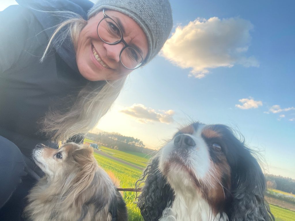 A woman, smiling, posing with two dogs outside
