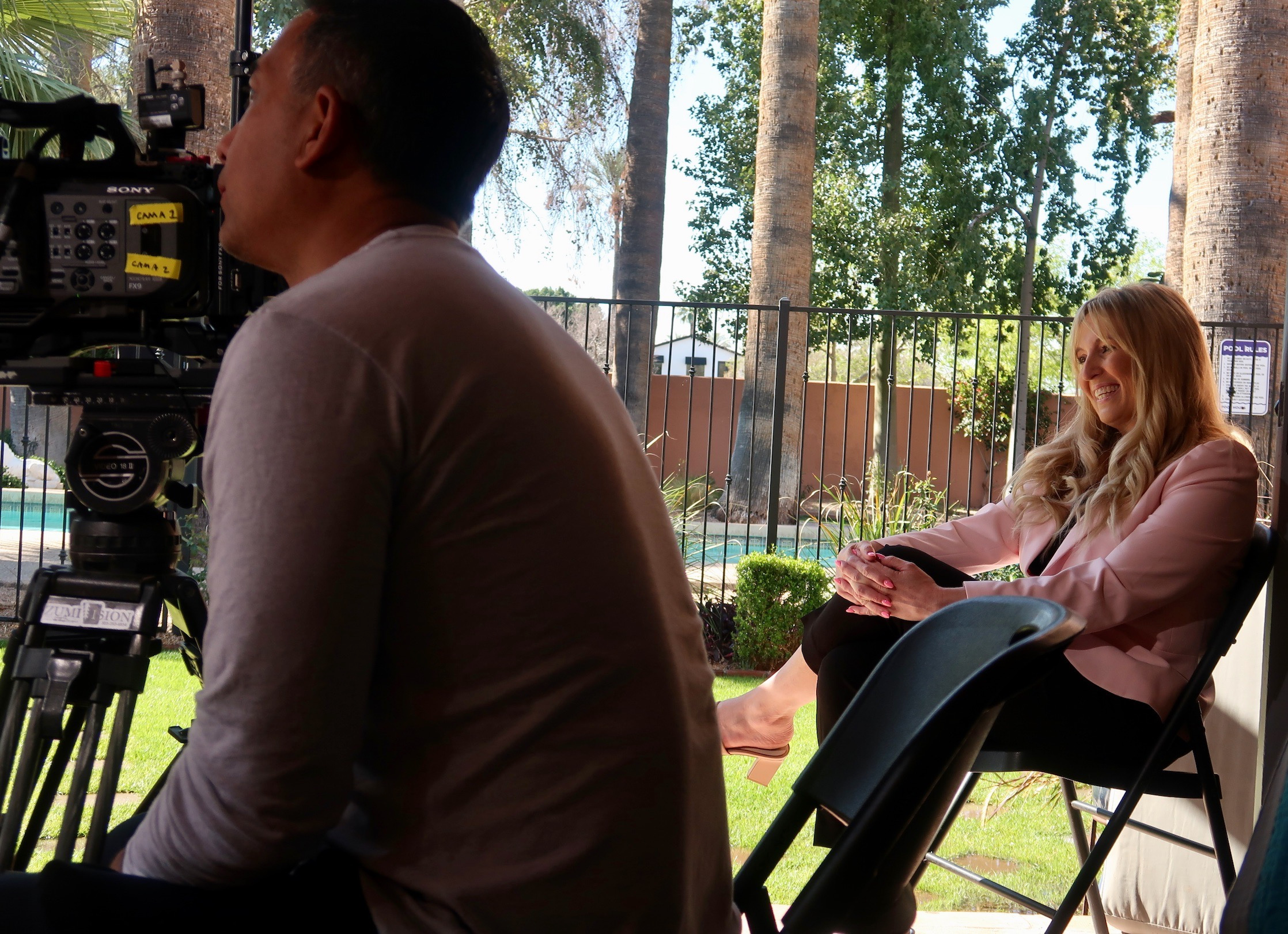 Rachel C. smiles while observing her mother being interviewed on camera.