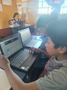 A teacher leading students in a lesson while they use a laptop.