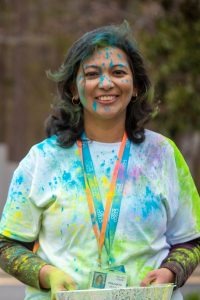 Woman facing camera smiling covered in colorful powder.